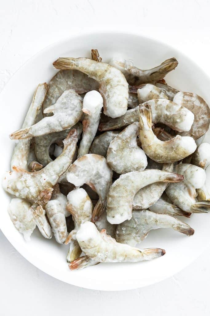 Frozen raw uncooked tiger shrimp on white stone surface, top view flat lay, square format