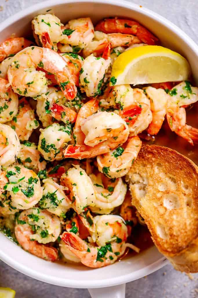 top view garlic butter shrimp in a white frying pan with bread and lemon