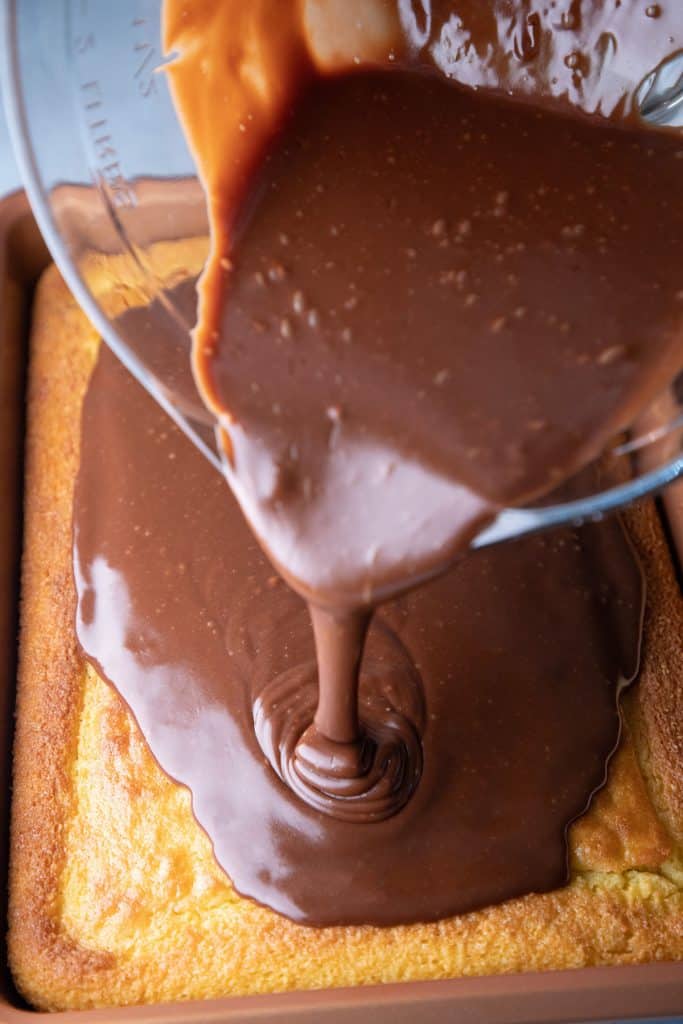 chocolate frosting being poured onto a sheet cake