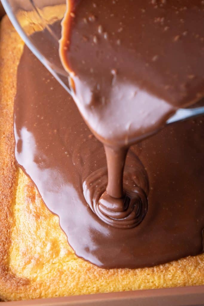 chocolate frosting being poured onto a sheet cake