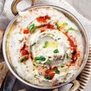 a plate of Baba Ghanouj garnished with olive oil, paprika and chopped parsley with bread next to it