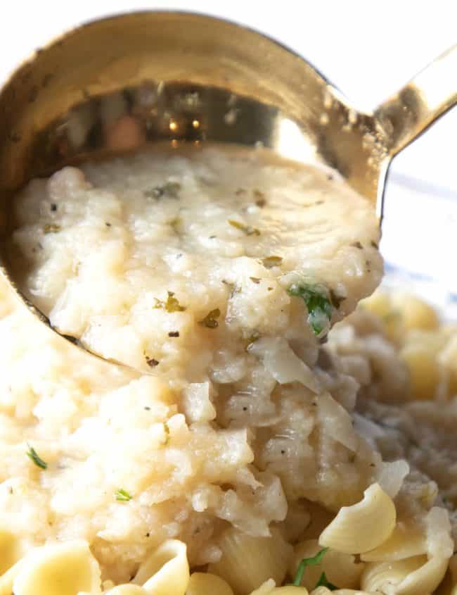 a spoonful of cauliflower sauce being added to a dish of pasta