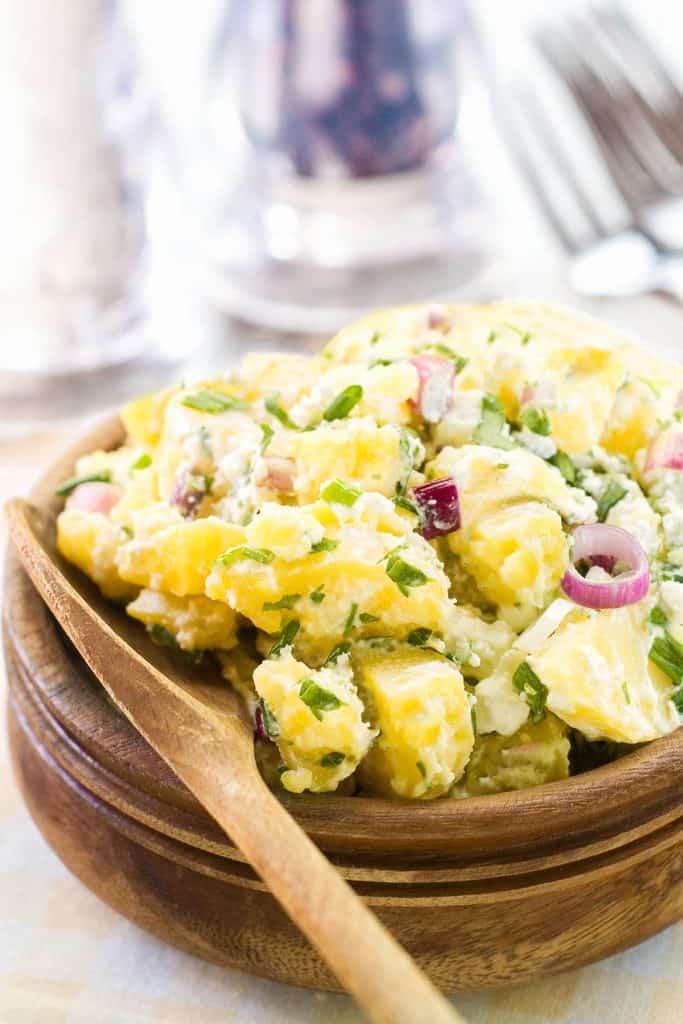 potato salad in a wooden bowl with a wooden spoon next to it and salt and pepper in the background