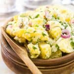 potato salad in a wooden bowl with a wooden spoon next to it.