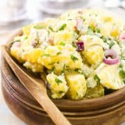 potato salad in a wooden bowl with a wooden spoon next to it.