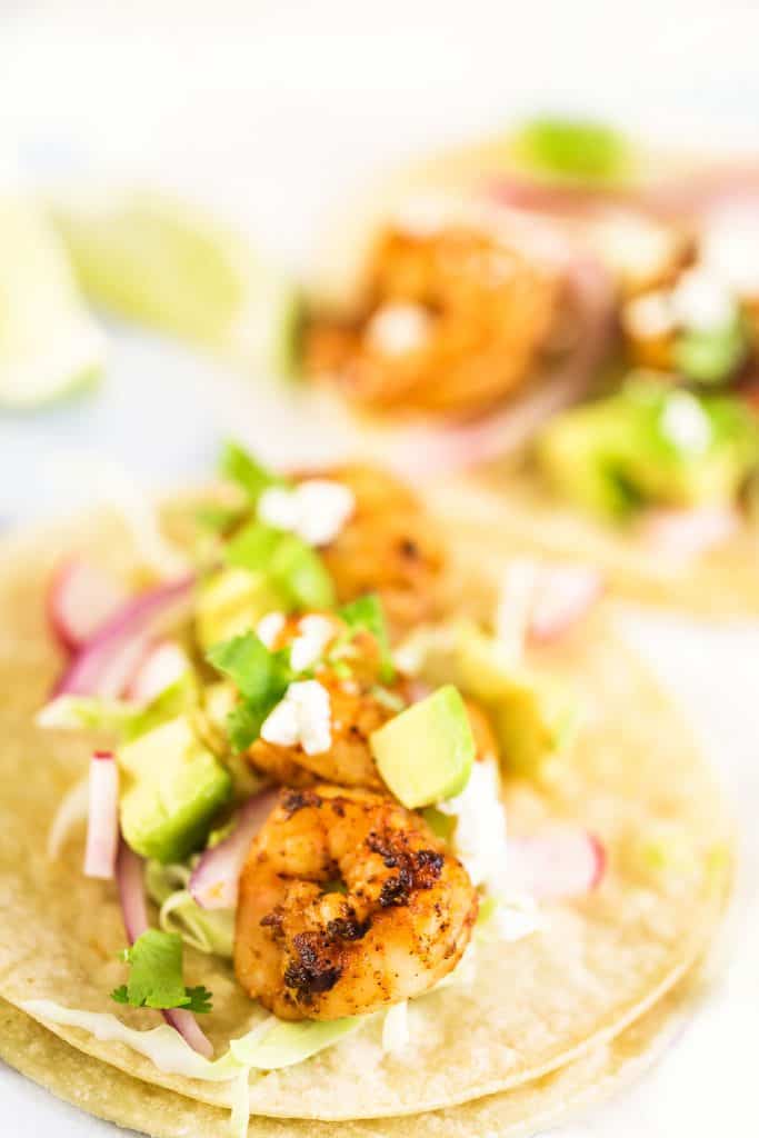 Fresh shrimp tacos with cotija cheese on a white corn tortillas.