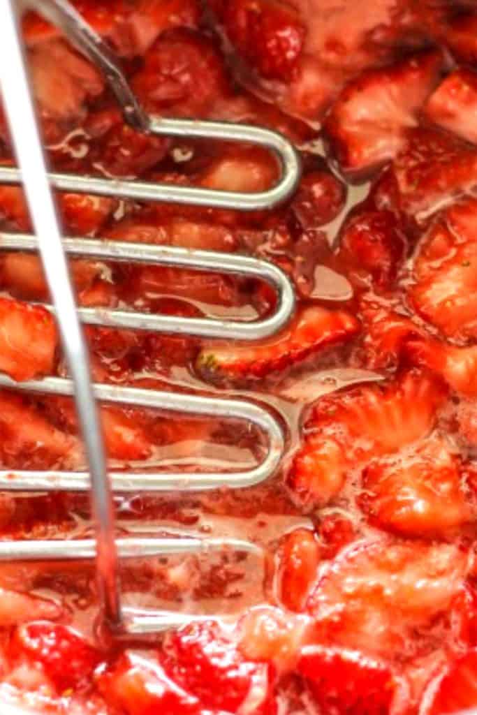 strawberries in a pan being mashed with a potato masher