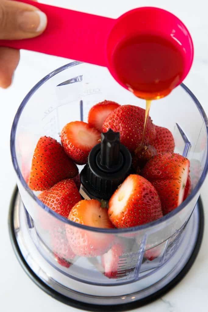 honey poured into blender with syrawberries