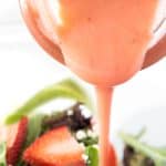 strawberry salad dressing being poured onto a salad.
