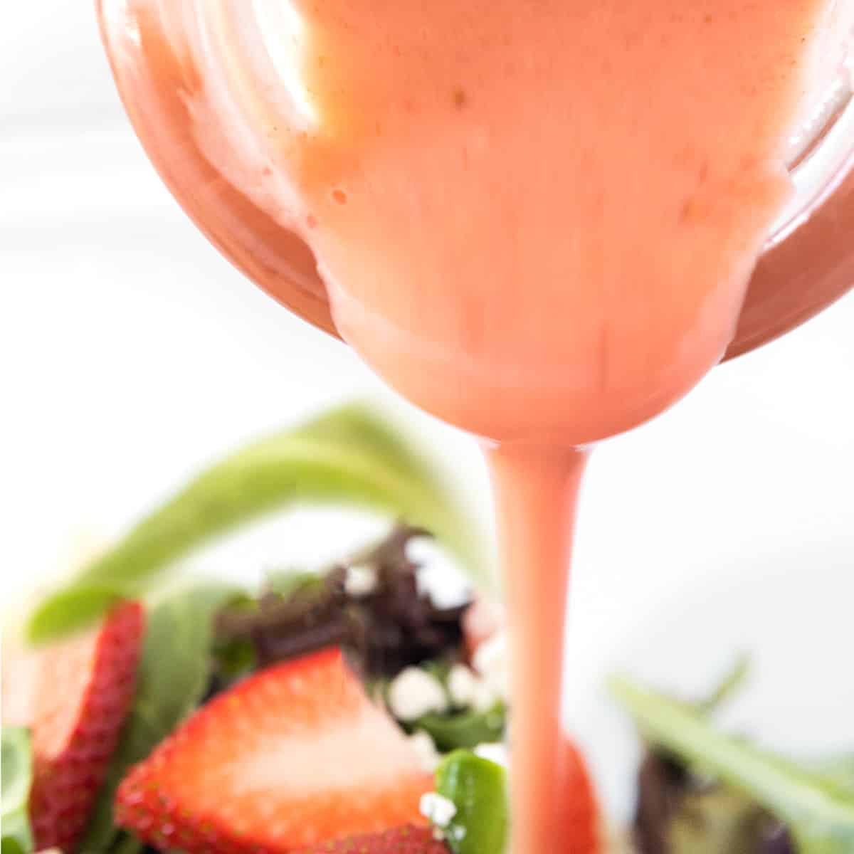 strawberry salad dressing being poured onto a salad.