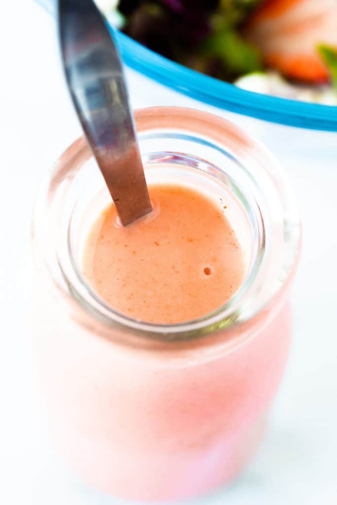 a jar filled with strawberry salad dressing with a spoon in it