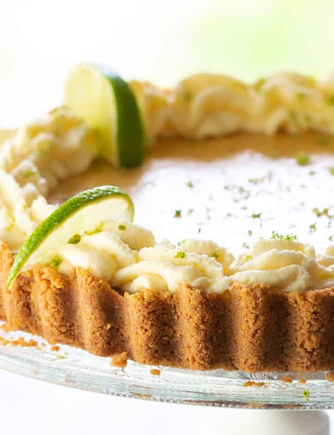 A key lime pie swirled with whipped cream around the edge and garnished with lime slices and zest.
