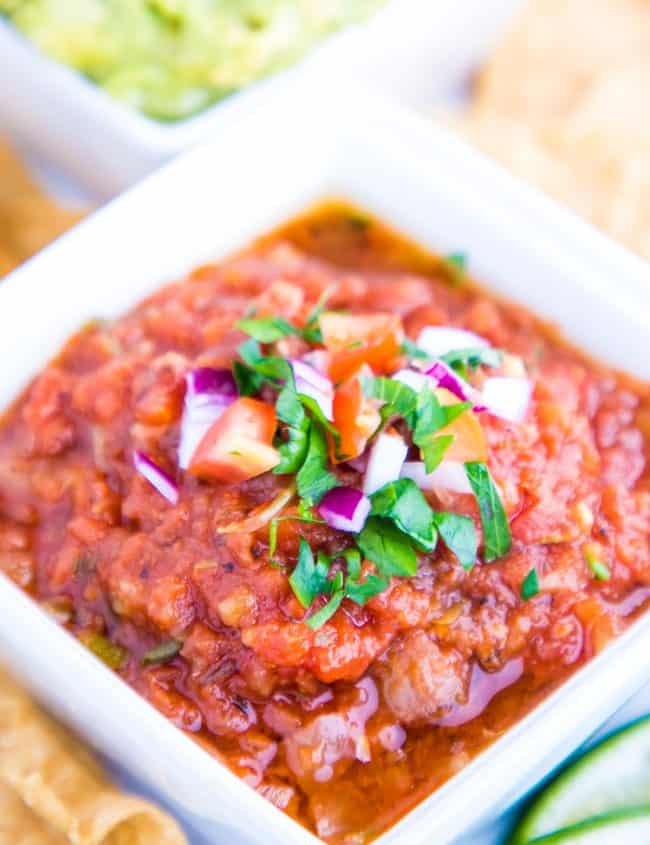 A close up of a bowl of salsa topped with raw onion and herbs