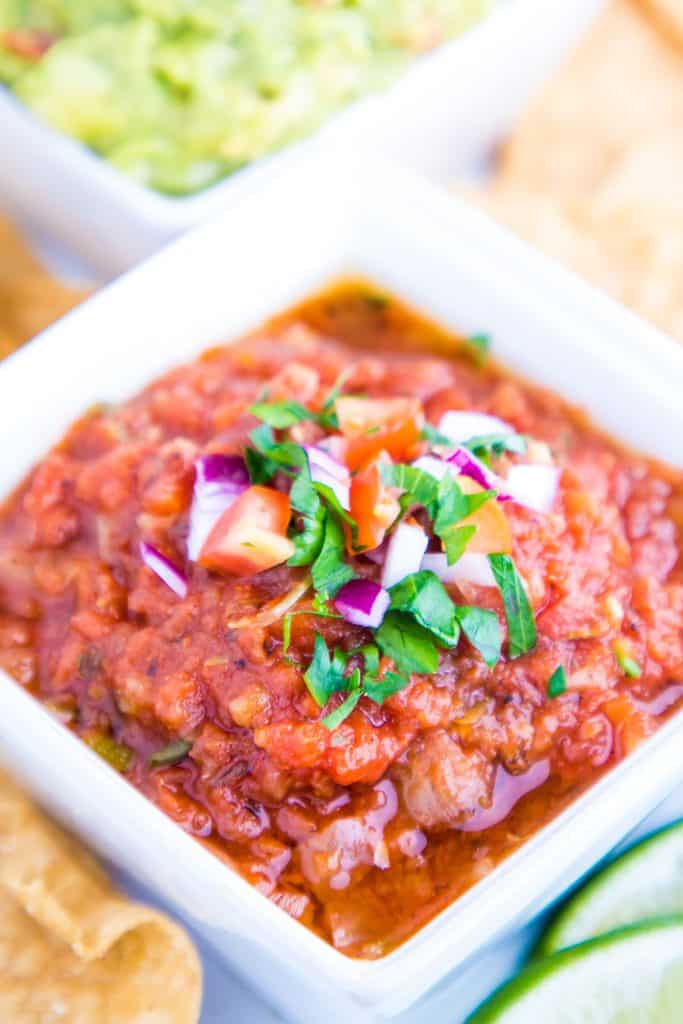 a close up of a bowl of salsa topped with raw onion and herbs