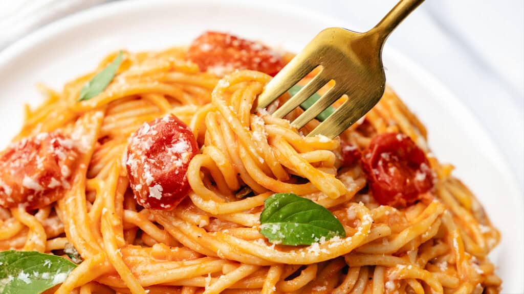 A white plate with a serving of spaghetti with tomato sauce and basil leaves.