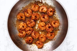 Cooked shrimp with seasoning in a circular arrangement in a pan, showing a golden-brown sear, ready to be served.