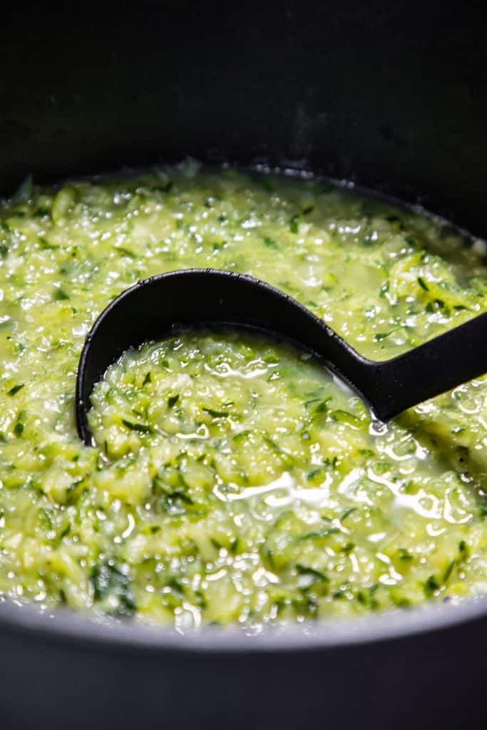 zucchini cooking in a pan with a ladle in it