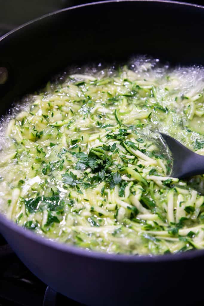 shredded zucchini in a pan with stock and garlic