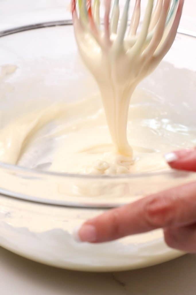 a whisk mixing icing in a glass bowl