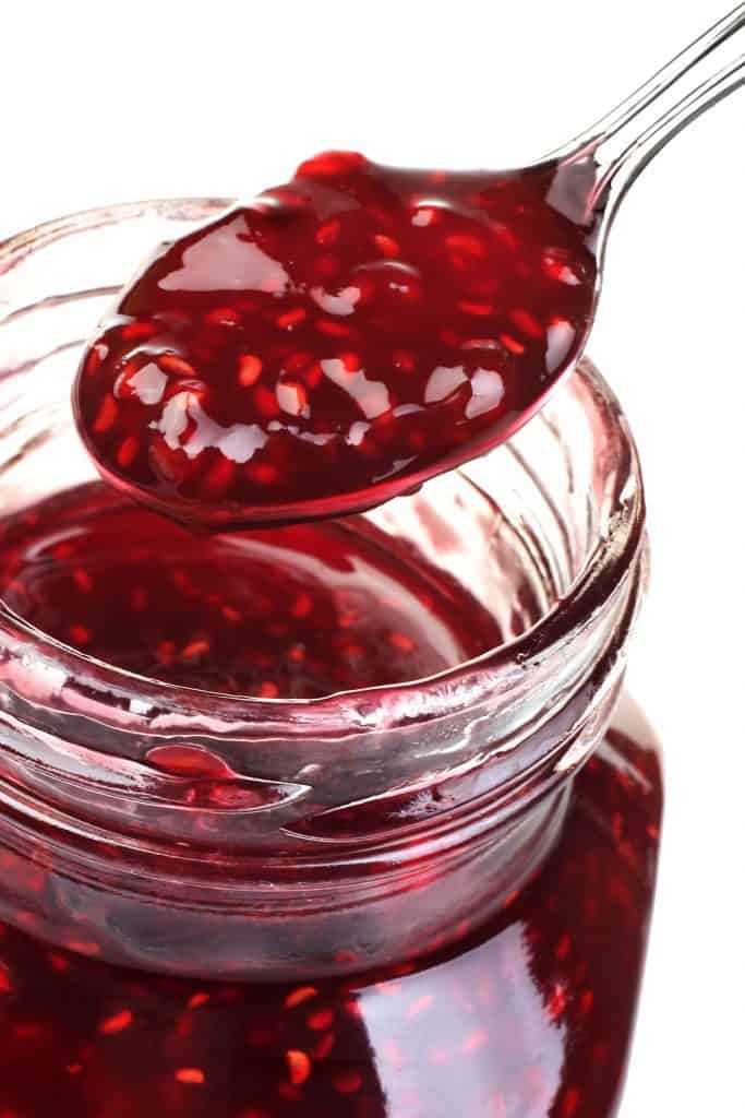 Raspberry Jam Preserves in glass with metal spoon isolated on white