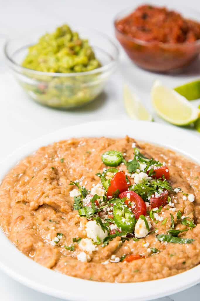 a bowl of refried beans topped with jalapenos, tomatoes, and crumbled cheese