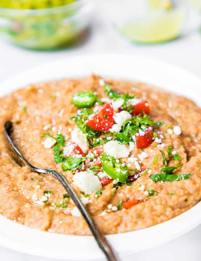 a spoon in a bowl of refried beans topped with jalapenos