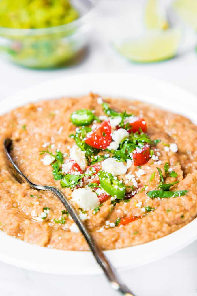 a spoon in a bowl of refried beans topped with jalapenos