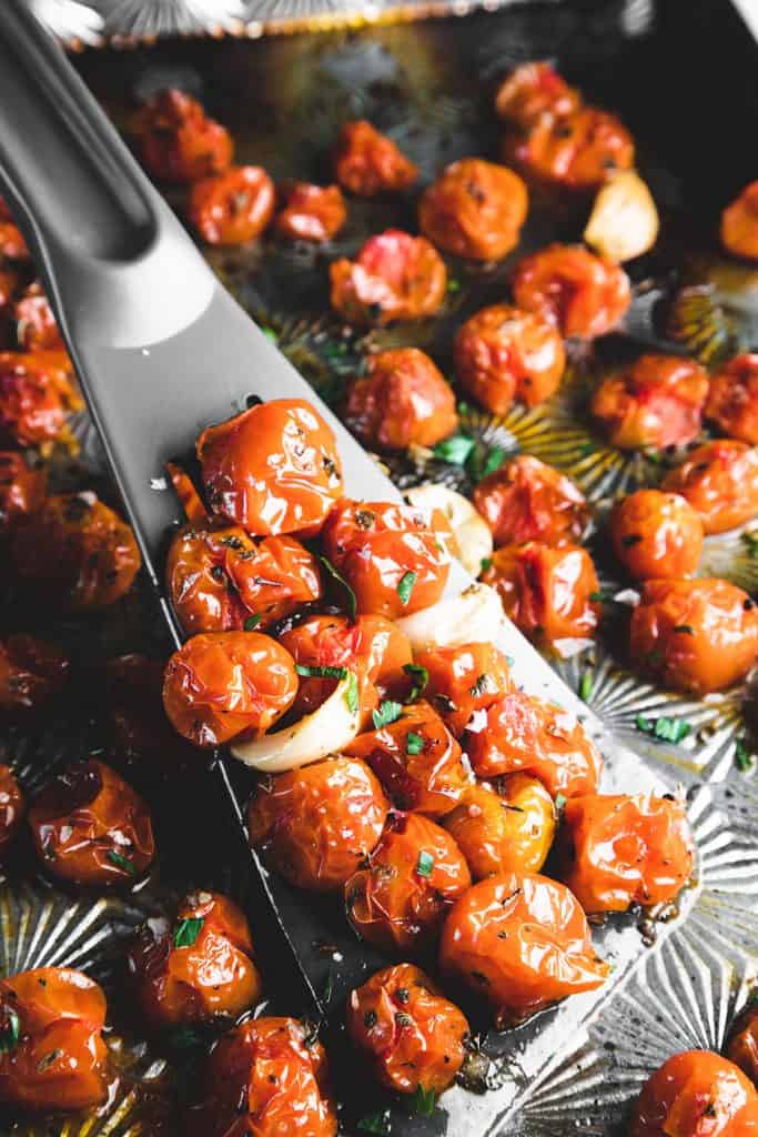 a spatula scraping tomatoes from an oven tray