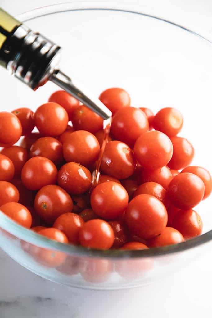 oil being poured onto a bowl of tomatoes