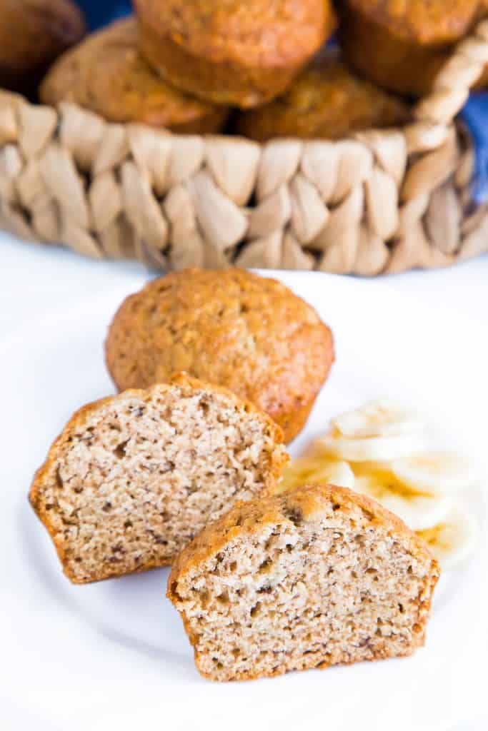 a muffin sliced in half with a basket of banana bread muffins behind it