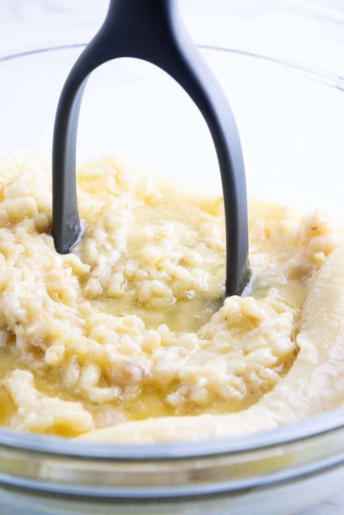 bananas being mashed with a potato masher