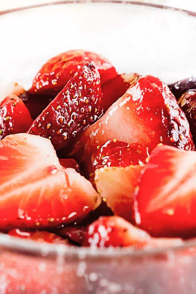 Close up of sliced strawberries in clear glass bowl glazed with