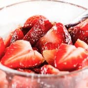 Close up of sliced strawberries in clear glass bowl glazed with