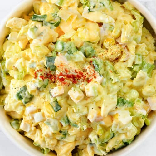 A bowl of creamy potato salad topped with paprika, featuring chunks of potatoes, green bell peppers, and hints of the Best Classic Egg Salad Recipe—all mixed with a rich mayonnaise-based dressing.