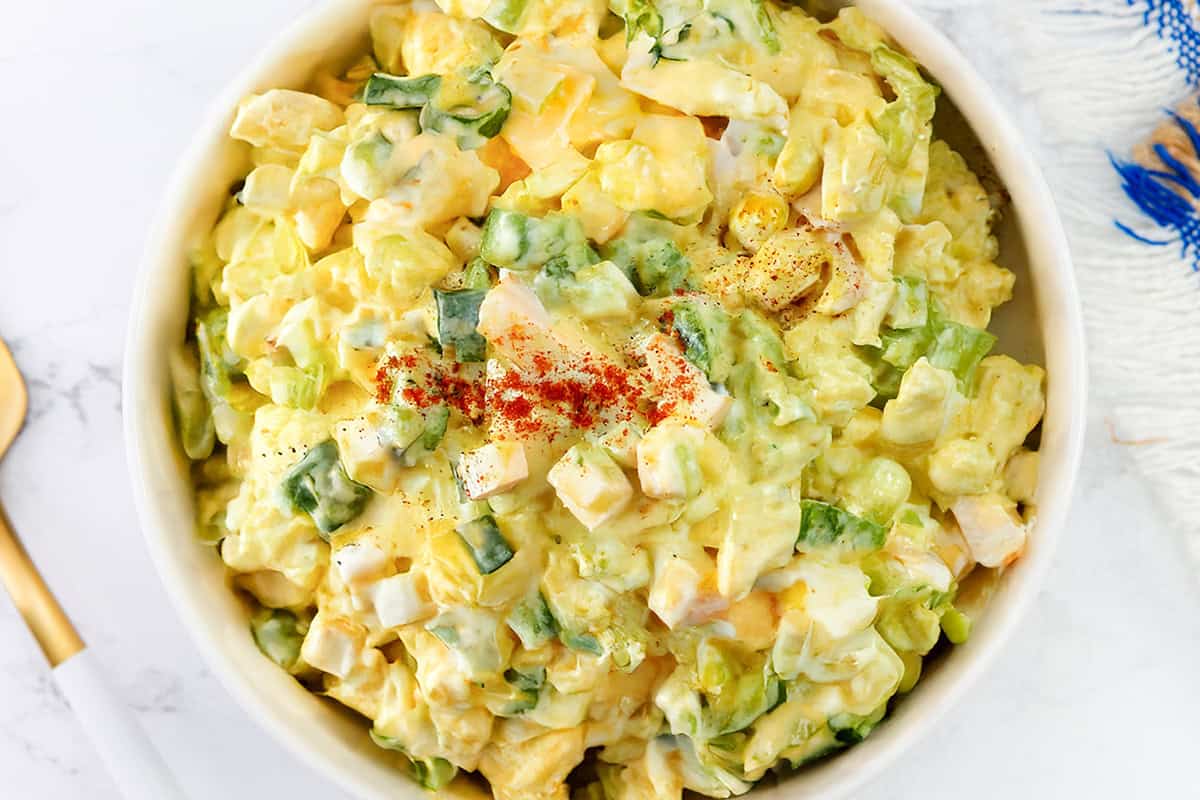 A bowl of creamy potato salad topped with paprika, featuring chunks of potatoes, green bell peppers, and hints of the Best Classic Egg Salad Recipe—all mixed with a rich mayonnaise-based dressing.