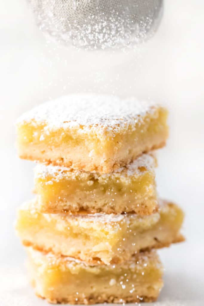 Close up view of a stack of lemon squares with powdered sugar being sprinkled on top.