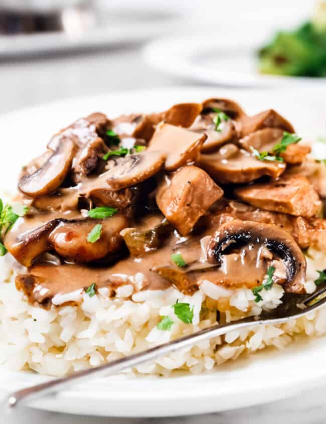 a close up image of Chicken Stroganoff on rice with a fork laying on the plate.