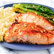 two pieces of garlic butter salmon with roasted asparagus and rice pilaf.
