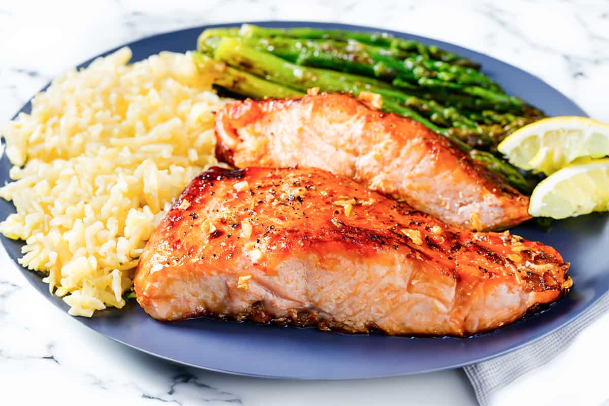 two pieces of garlic butter salmon with roasted asparagus and rice pilaf.