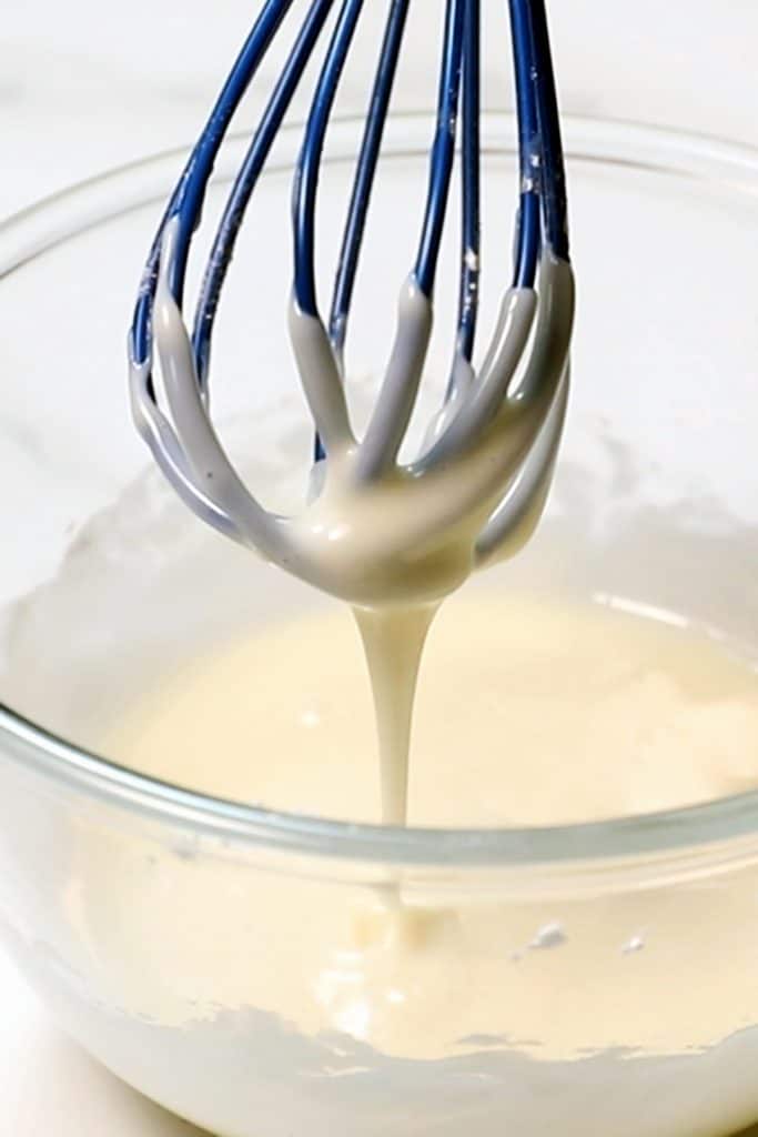 Lemon icing running through a whisk into a bowl