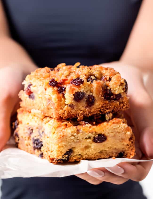 a woman holding two Oatmeal Raisin Bars on baking paper.