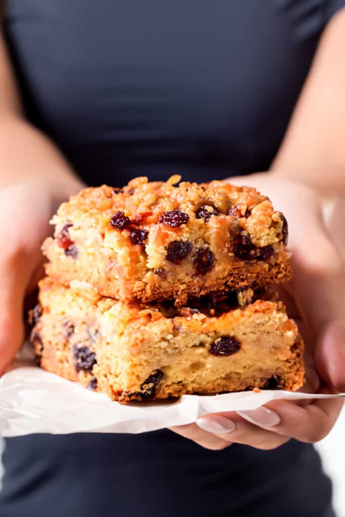 a woman holding two Oatmeal Raisin Bars on baking paper.