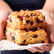 a close up image of a woman holding two Oatmeal Raisin Bars on baking paper.