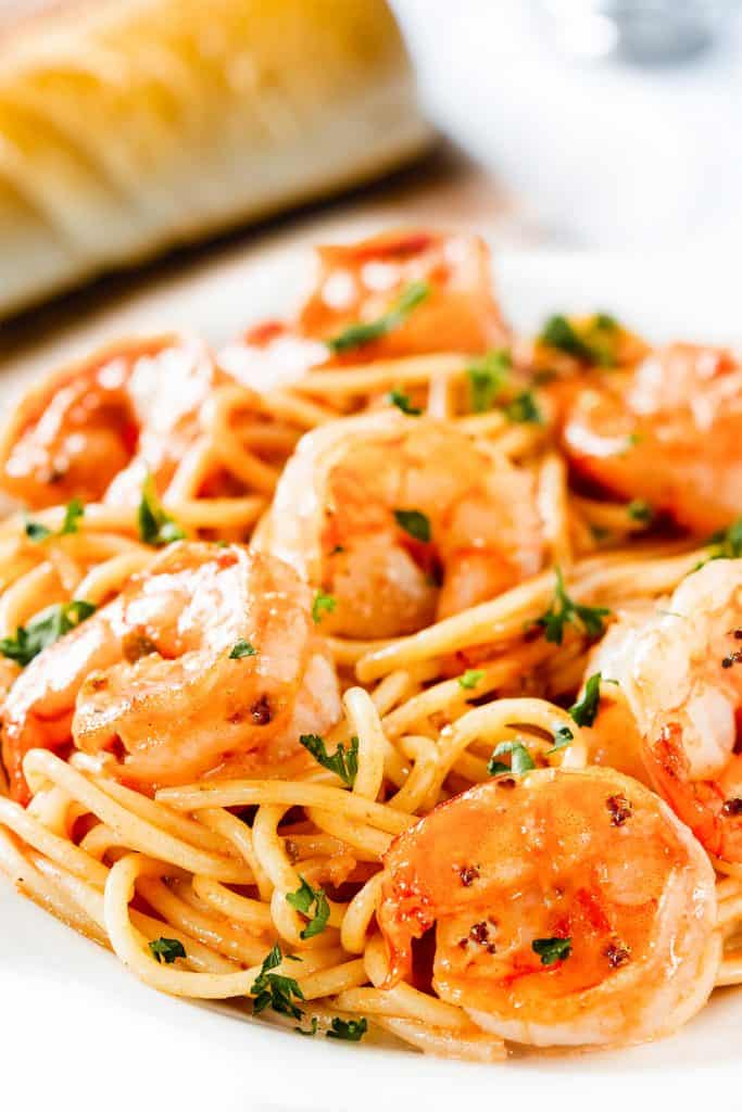 shrimp and spaghettion a plate with bread in the background