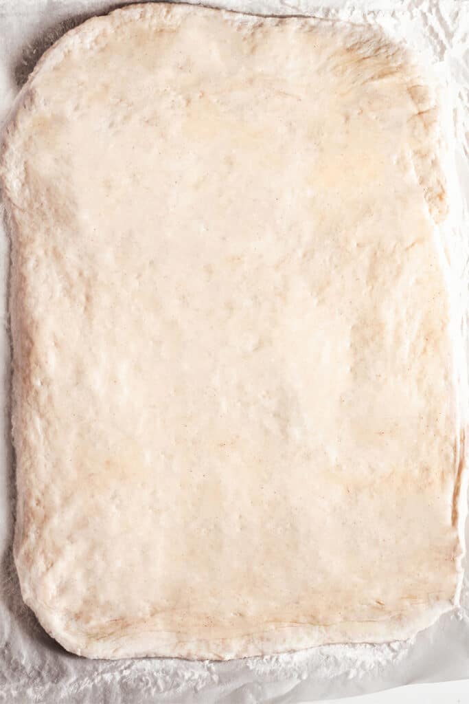 the rolled dough for making Cinnamon Rolls With Apple Pie Filling on a floured surface.