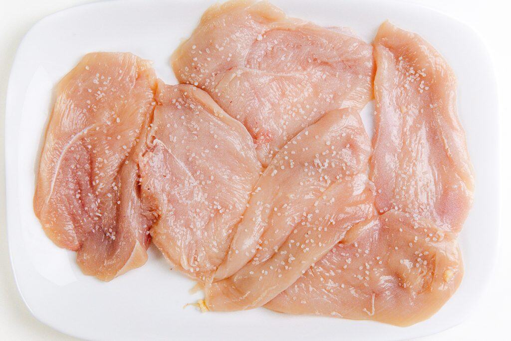 Raw chicken breast slices arranged on a white plate, sprinkled with coarse salt—ideal for preparing classic Chicken Marsala.