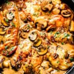 A close up image of A cast iron pan filled with chicken marsala and mushrooms.