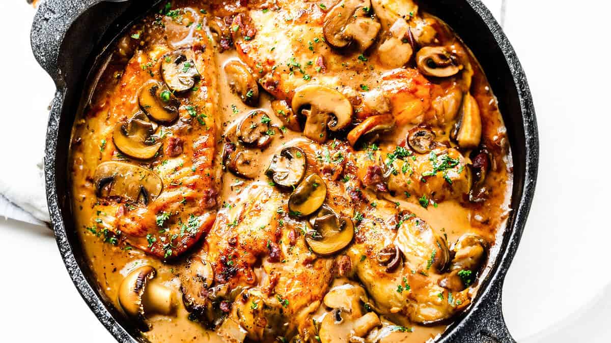 a close up image of A cast iron pan filled with chicken marsala and mushrooms.