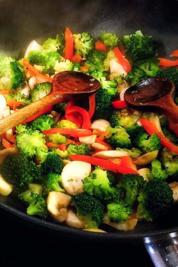 broccoli being added to the pan with peppers and chicken