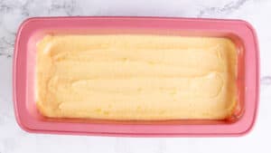 Smooth lemon pound cake batter evenly spread in a pink loaf pan, ready to be baked.